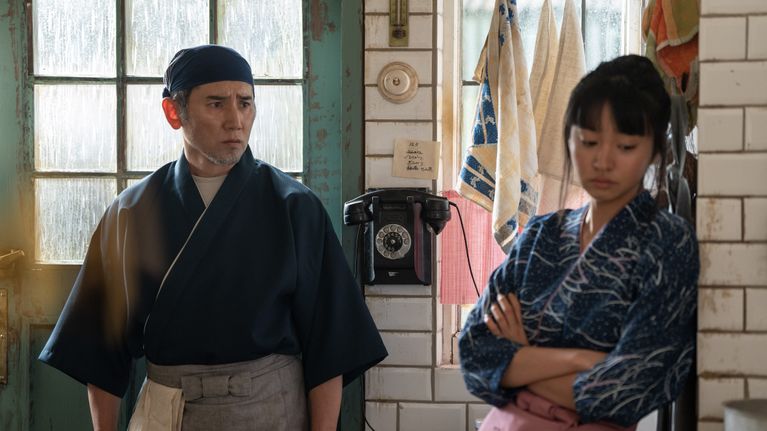 Vanhempi japanilainen mies katsoo nuorempaa japanilaista naista, joka katsoo alas.