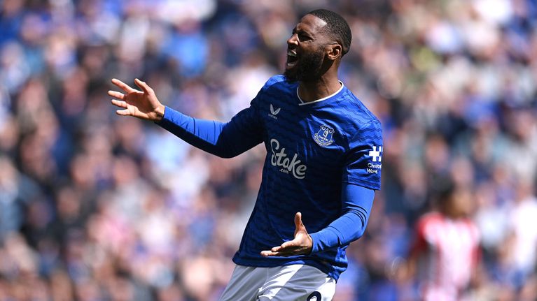 En fotbollsspelare i Evertons blå matchtröja med nummer 9 och texten "Stake.com" sträcker ut armarna på planen.
