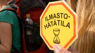 Sormet kannattelevat kylttiä, jossa lukee "Ilmastohätätila."