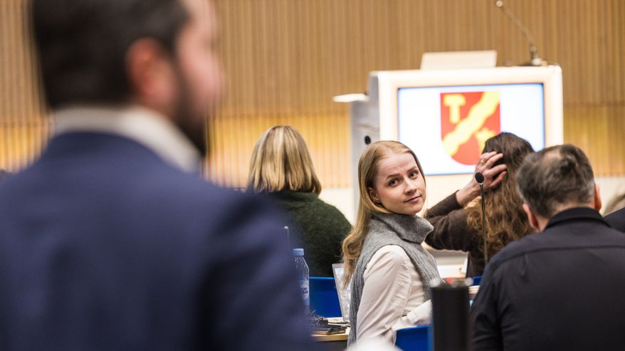 Nainen kääntyy katsomaan paperin kanssa puhuvaa miestä poliittisessa kokouksessa.