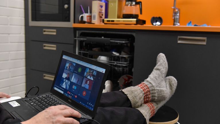A man wearing woolen socks, feet up, holding a laptop, in a virtual meeting