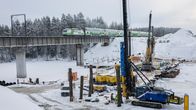 Juna rautatiesillalla, joka ylittää jäisen salmen. Viereen rakennetaan uuden sillan perustuksia suurilla koneilla.
