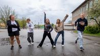En vuxen och fyra barn poserar på en skolgård.