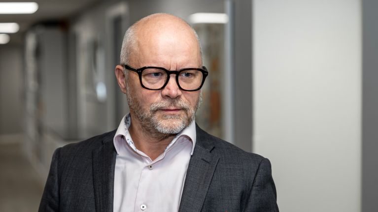 Silmälasipäinen mies katsoo oikealle.