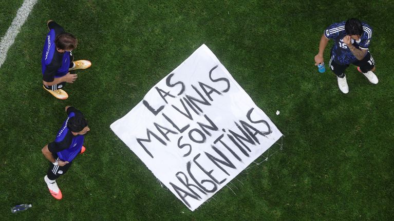 Jalkapalloilijat seisovat Las Malvinas son Argentinas -tekstin sisältävän lakanan ympärillä.