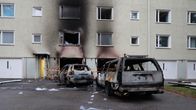 Kerrostalon alakerroksen ovet ja ikkunat ovat mustuneet tulipalossa, pihalla seisoo kaksi täysin palanutta autoa.