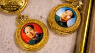 Kaksi kultaista taskukelloa, joiden kansissa on Mao Zedongin värilliset muotokuvat punaisella ja sinisellä taustalla.