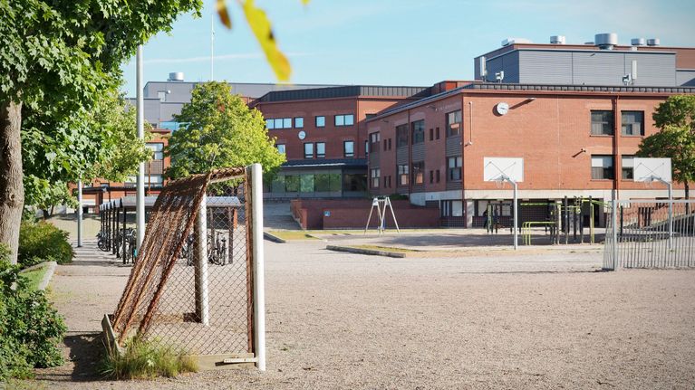 Turun Normaalikoulus skolgård med basketkorgar och klätterställning framför en röd tegelbyggnad, inga personer syns.