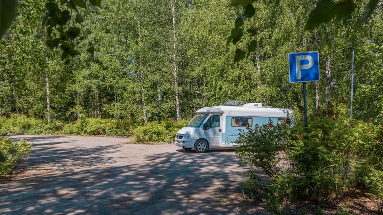 Asuntoauto parkkipaikalla. Takana metsää.