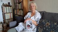 En kvinna sitter i en soffa med en bok i knät. I bakgrunden står bokhyllor med böcker.
