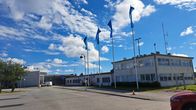 Vaasan lentoaseman vaaleat rakennukset, pihalla viisi lippua lipputangoissa ja muutama auto pysäköitynä.