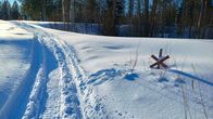 Moottorikelkan jälki hangella ja vieressä kelkkareitin risteyksen merkki.