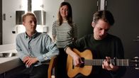 Porträtt på bandet Vasas flora och fauna. Mattias Björkas håller gitarr i famnen. Tina Kärkinen ler. Daniel Ventus ser allvarlig ut. 
