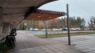 Sairaalan pääsisäänkäynnin ovella on pyöriä ja parkkipaikalla autoja.