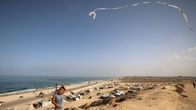 En pojke flyger drake ovanför flyktingtält på stranden i Gaza. 