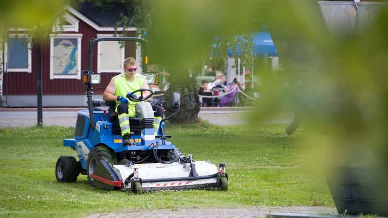 Mies ajaa ruohonleikkuria puistossa kaupungissa.