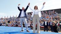Tim Walz ja Kamala Harris seisovat vierekkäin lavalla kädet ylhäällä pitäen toisiaan kädestä kiinni. Taustalla yleisöä Yhdysvaltain lippujen ja kampanjakylttien kanssa.