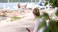Henkilö istuu penkillä piensatamassa tutkien puhelintaan.