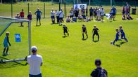 Unga fotbollspelare och åskådare på en solig fotbollsplan.