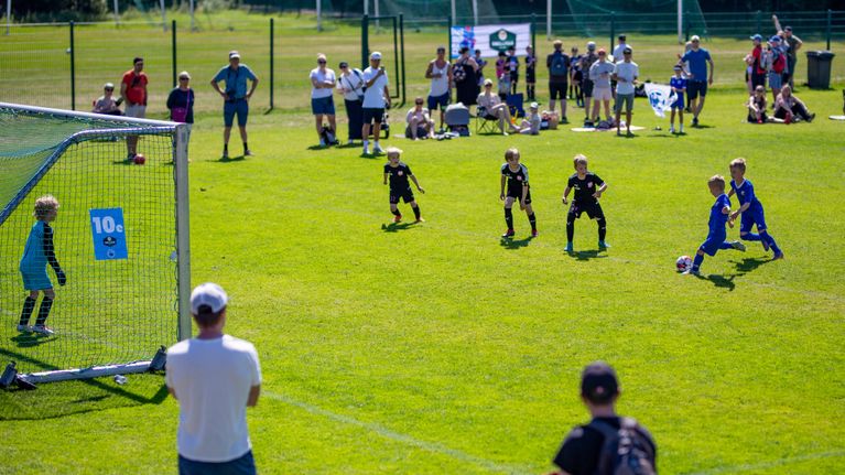 Unga fotbollspelare och åskådare på en solig fotbollsplan.