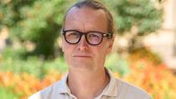 Professor Johan Strang fotograferad på universitets innergård. Han är ledigt klädd i en skjorta och bakgrunden är somrig.