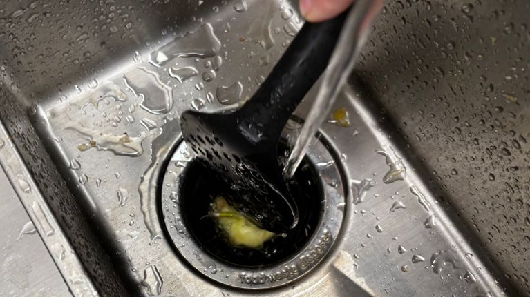 Käsi työntää paistolastalla omenaa tiskipöydän altaassa olevaan biojätemyllyyn.