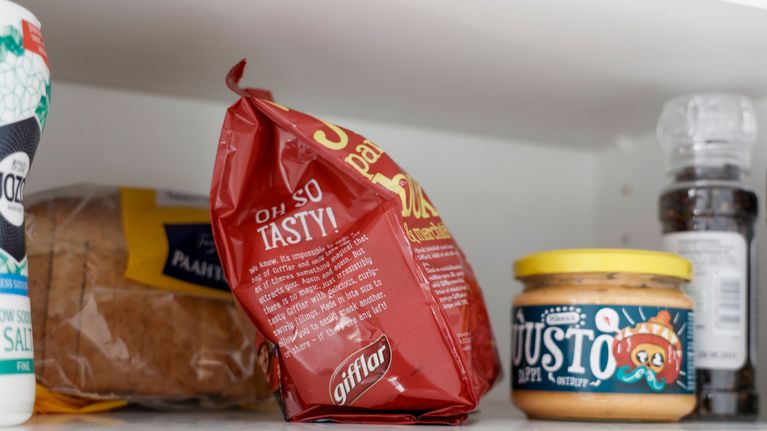 Keittiön hyllyllä leipäpaketti, punainen gifflar-pussi, juustolevitepurkki, suolaa ja pippurimylly.