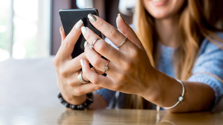 Woman holding a smartphone with both hands and smiling.