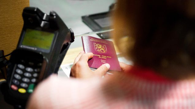 A person holds a Finnish passport in their hand at a police service counter.