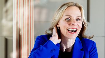 istuu sisätiloissa sinisessä jakussa, katse kohti kameraa.