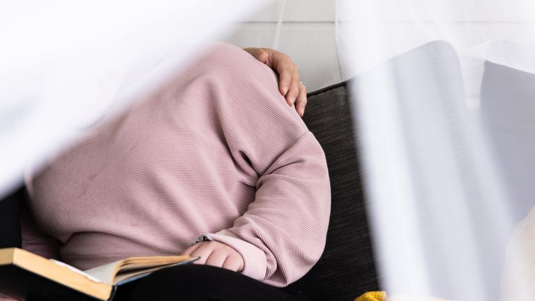 Kaksi henkilöä istuu sohvalla; toisella on vaaleanpunainen paita ja avattu kirja kädessä, toinen laskee käden hänen olalleen.