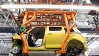 Kirkkaankeltainen autonrunko robottikäsien varassa. Renkaat, ovet, ikkunat puuttuvat.