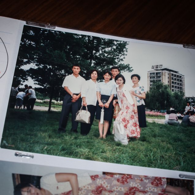 Sex personer står på gräs framför träd; ett fler-våningshus med koreansk text syns i bakgrunden. "1996" och handskrivet till vänster.