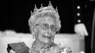 Prinsessa Astrid istuu pöydän ääressä, käyttää kruunua ja juhla-asua. Taustalla näkyy hämärästi toinen henkilö.