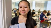 Thy "Anna" Nguyen seisoo luokkahuoneen ovella ja hymyilee kameralle. Taustalla näkyy yo-kokeen valmisteluhetkiä.