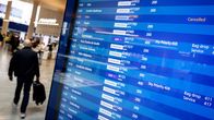 An airport departures screen showing that a Finnair flight to Doha has been cancelled. In the background, a person is carrying a suitcase.