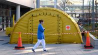 Ett gult tält utanför Karolinska universitetssjukhuset och en sjukskötare som går förbi. 