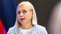 Elina Valtonen seisoo puhujapöntön takana mikrofonin edessä, taustalla Saksan ja Suomen liput.