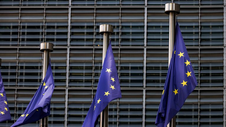 Kolme Euroopan unionin lippua liehuu lipputangoissa nykyaikaisen rakennuksen edessä.
