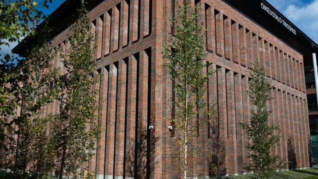 A massive red-brick building with a few birch trees in front and a sign saying 'Courthouse' in Finnish and Swedish.