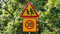 Liikennemerkissä 30:n nopeusrajoitus ja huomautus lapsista. Taustalla puita täynnä lehtiä.