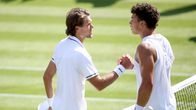 Kaksi tennispelaajaa kättelee verkolla ruohokentällä ottelun jälkeen, molemmat valkoisissa urheiluvaatteissa.