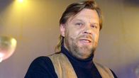 Vesa-Matti Loiri katsoo kameraan, hänellä on yllään tummansininen poolopaita ja ruskea mokkanahkaliivi.