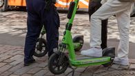 Kaksi miestä sähköptkulaudoilla ja poliisi jalkakäytävällä. Kuvassa näkyy henkilöiden jalat. Sähköpotkulautaratsia.