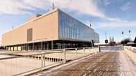 Pyörätien silta, jossa valkeat metallikaiteet. Taustalla betoninen talo, jonka seinässä teksti TEATTERI.