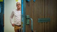 Julkisen sanan neuvoston kyltti tammiovessa, taustalla oviaukossa puheenjohtaja Eero Hyvönen sumeana.