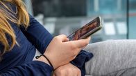 Närbild på en person med långt hår som sitter och håller i en mobiltelefon.