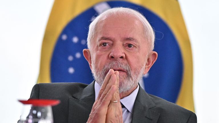 Brasilian presidentti Luiz Inacio Lula da Silva pitää käsiään yhdessä Brasilian lipun edessä.