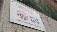 Valkoinen kyltti talon seinässä. Kyltissä teksti ELOISE GILLOW. Käännekohta, 2022. Oulu 2026. EUROOPAN KULTTUURIPÄÄKAUPUNKI.