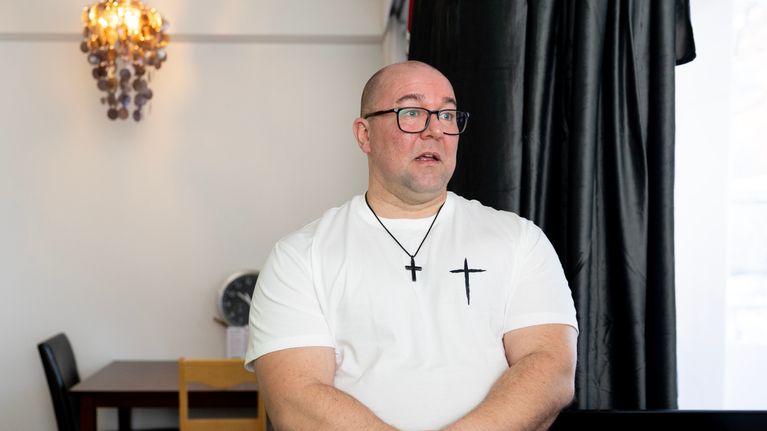 Mies seisoo valkoisessa paidassaan keittiön pöytä takana. 